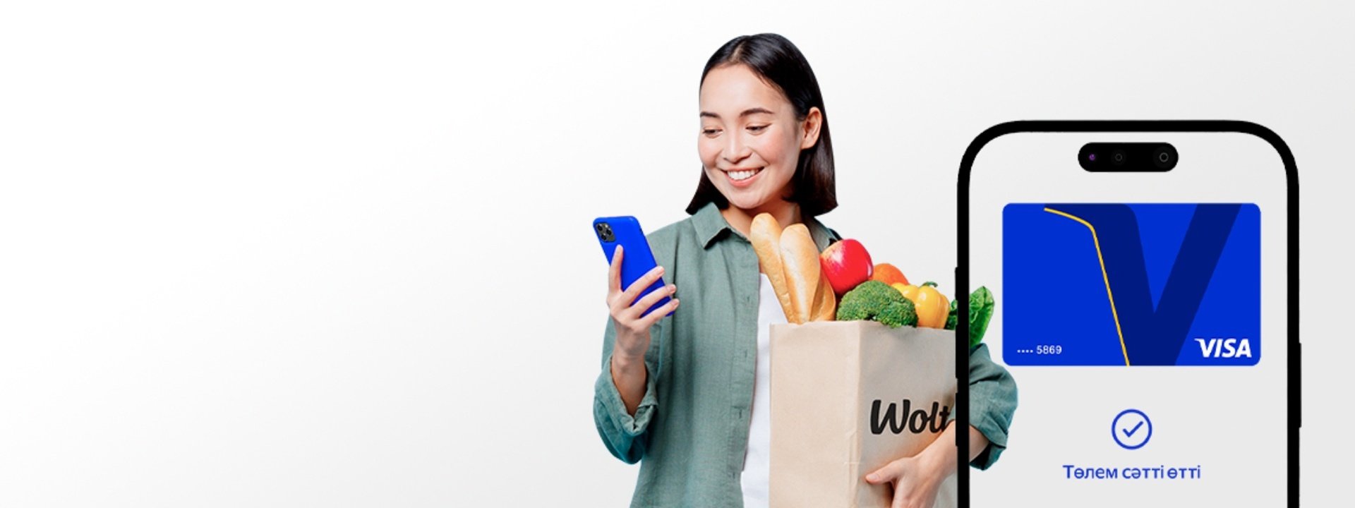 Smiling woman holding Wolt grocery bag and smartphone with successful Visa payment confirmation on screen.
