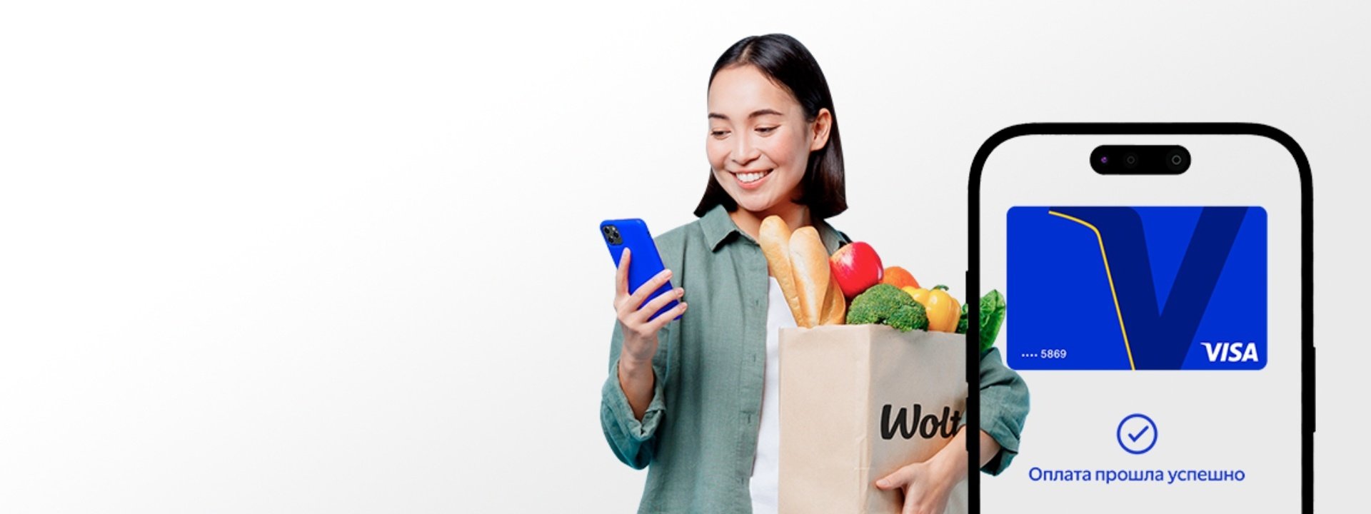 Smiling woman holding Wolt grocery bag and smartphone with successful Visa payment confirmation on screen.