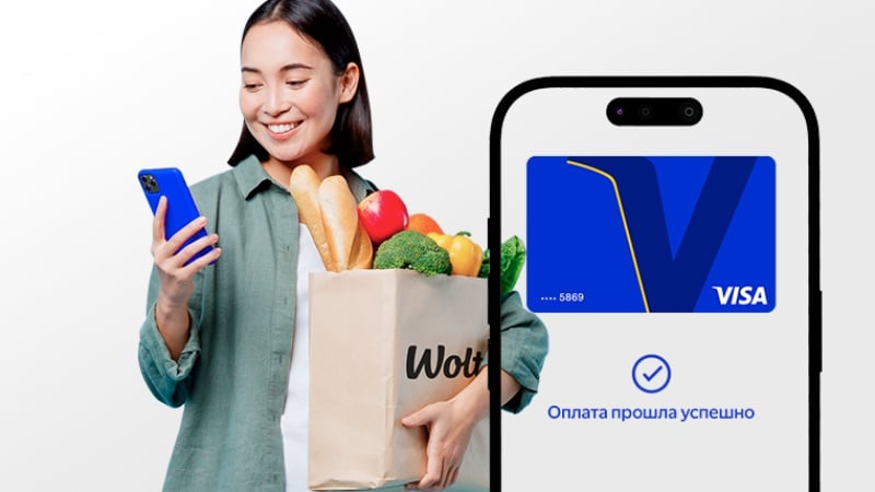 Smiling woman holding Wolt grocery bag and smartphone with successful Visa payment confirmation on screen.