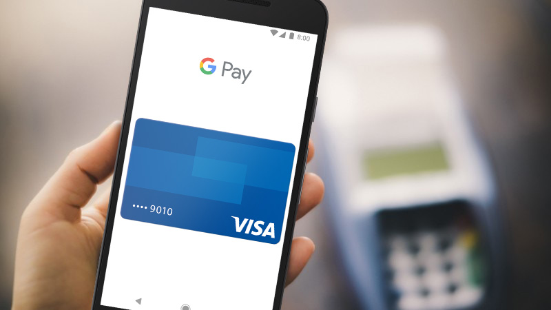 Google Pay с Visa на телефоне с Android Hand holding a mobile phone with Google Pay Visa card shown on the screen.