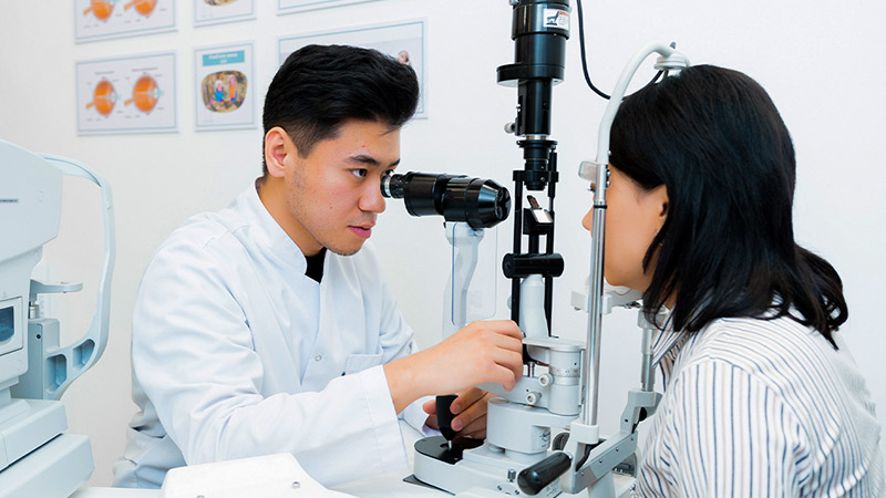 A healthcare professional conducts an eye examination for a patient using a slit lamp in a clinical setting.