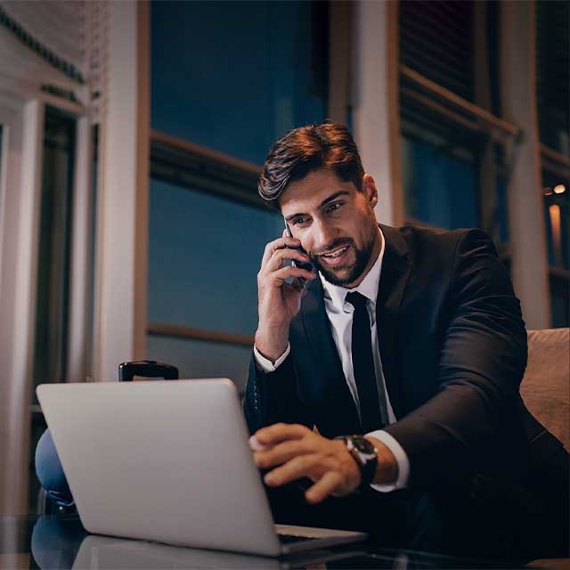 A man in the lounge zone talking on the phone and typing on his laptop