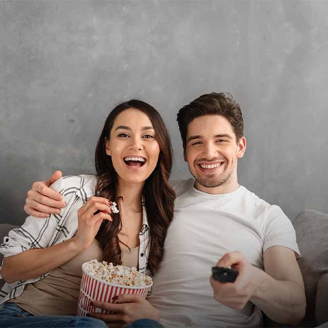 A man and a woman watching TV and eating popcorn