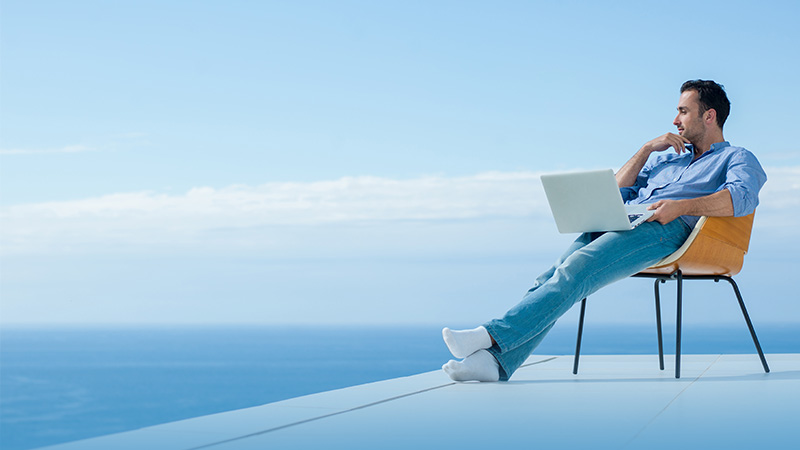 A man with a laptop sitting on the chair near the sea shore