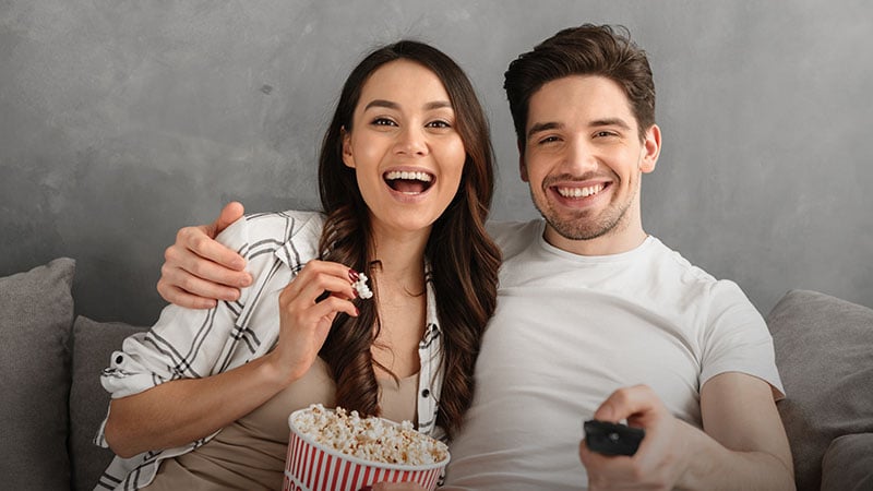A man and a woman watching TV and eating popcorn